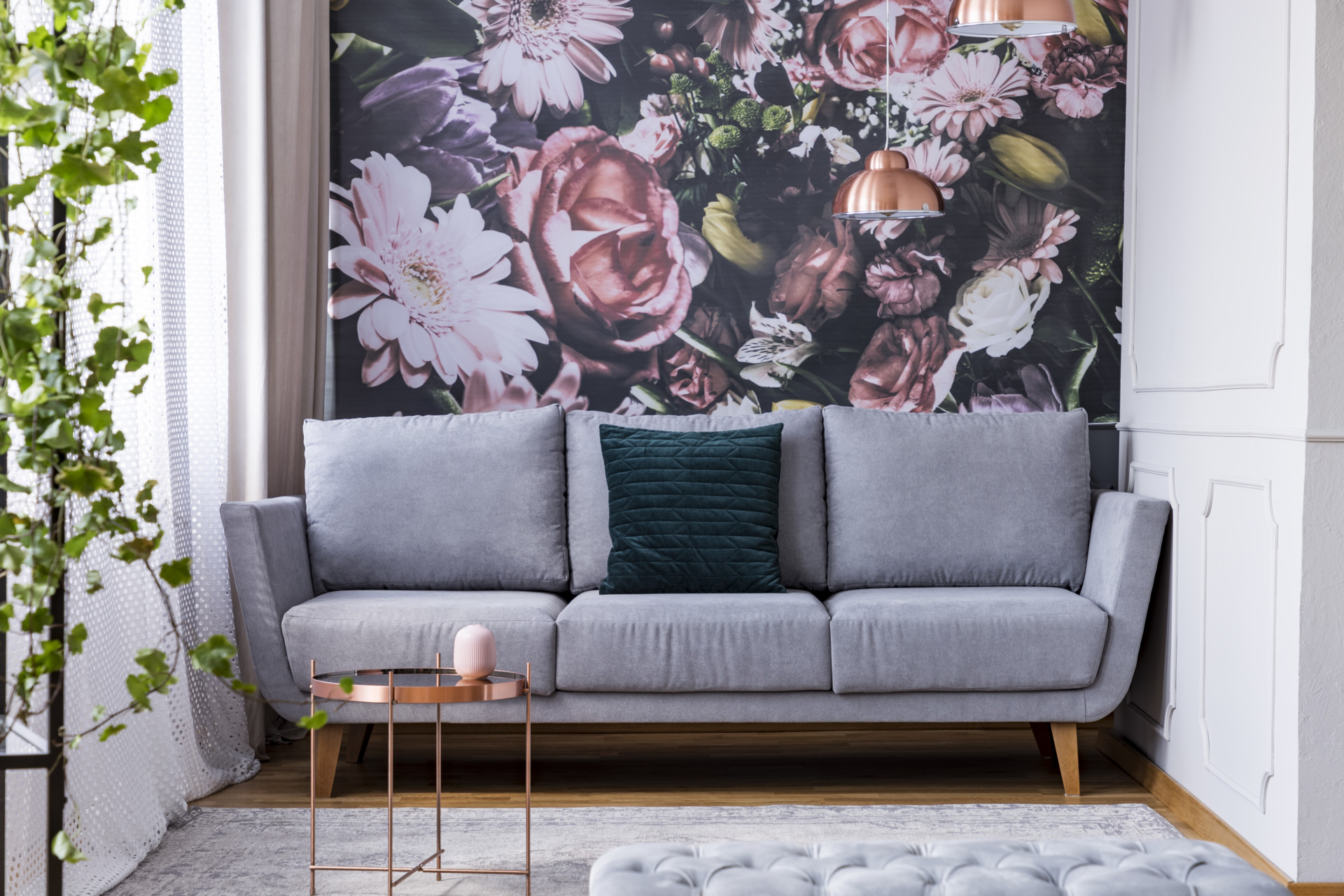Copper table on carpet and green pillow on grey couch in flowers living room interior. Real photo